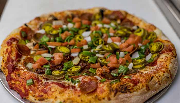 A Cadence Clubhouse pizza topped with pepperoni, diced tomatoes, onions, and sliced jalapeños.