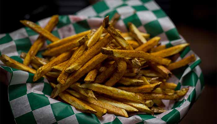 Golden french fries from the Cadence Clubhouse food menu in a checkered paper-lined basket.