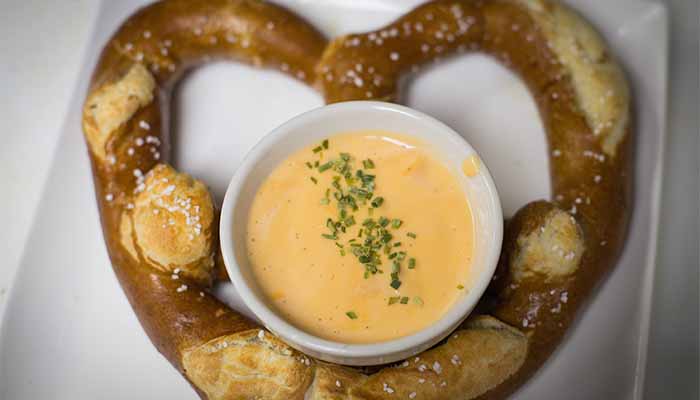 A heart-shaped soft pretzel from the Cadence Clubhouse menu with a bowl of herb-topped cheese dip.