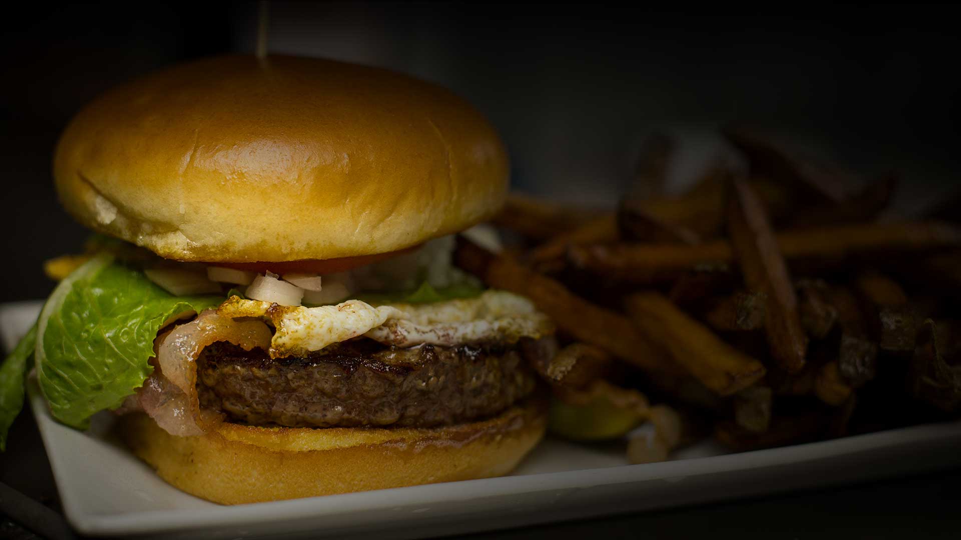 A burger with a fried egg and bacon, served with a side of fries.